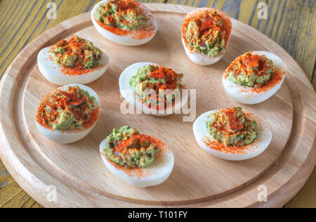 Guacamole and bacon deviled eggs on cutting board Stock Photo