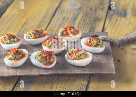 Guacamole and bacon deviled eggs on cutting board Stock Photo