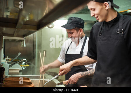 Enjoying work. Two smiling young chef assistants are working in a restaurant kitchen. Cooking concept Stock Photo