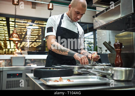 Important ingredient. Concentrated young chef breaking an egg for traditional italian pasta while standing in a restaurant kitchen. Cooking process Stock Photo