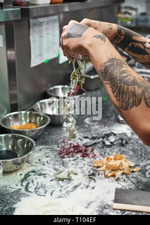 Traditional recipe. Cropped vertical image of chef's hands with beautiful tattoos making traditional italian pasta in restaurant kitchen. Food concept. Stock Photo