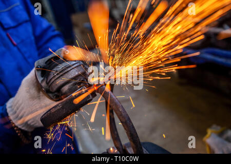 A close-up of a car mechanic using a metal grinder to cut a car bearing  in an auto repair shop, bright flashes flying in different directions, in the Stock Photo