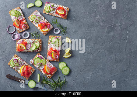 crispbread open-faced sandwich with smoked trout, soft cream cheese, cucumber, red onion, sprinkled with flax seeds on a concrete table, view from abo Stock Photo