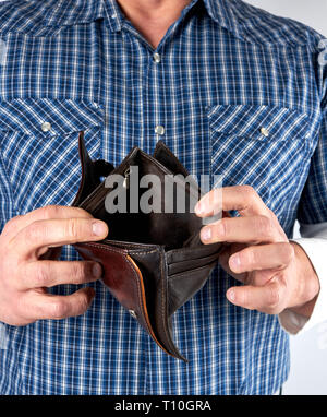 man in blue plaid shirt holds open empty leather wallet, poverty concept Stock Photo