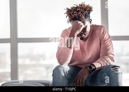 Thoughtful dark-skinned man sitting on cozy sofa Stock Photo