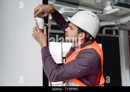 serious firefighter in uniform and helmet checking fire alarm Stock Photo