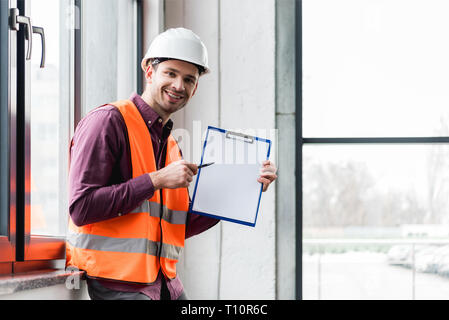 cheerful fireman in helmet and uniform holding clipboard with blank paper Stock Photo