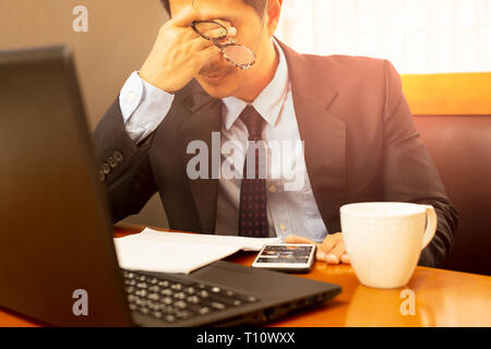 Stress businessman holding eyeglasses rubbing his eyes after long working hours. Stock Photo
