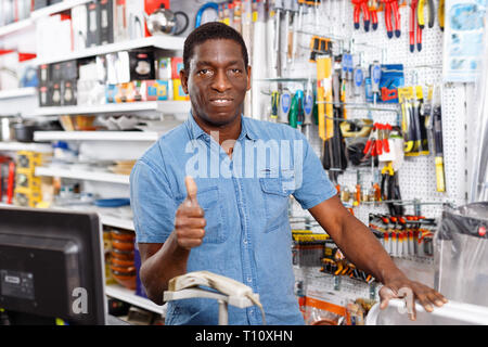 Portrait of smiling happy successful owner of household goods store standing behind counter, giving thumbs up Stock Photo