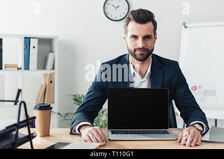 handsome advisor in suit showing laptop with blank screen at office Stock Photo