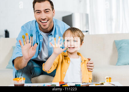 happy father and son looking at camera and showing painted hands at home Stock Photo