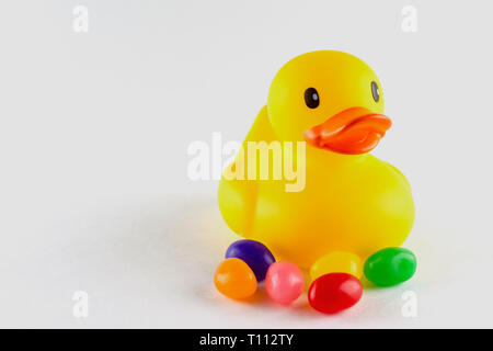 Close up of a toy rubber duck with a few jelly beans in front.  Isolated on white.  Copy space on the left. Stock Photo