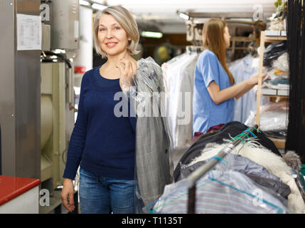 Portrait of cheerful female laundry customer holding clean clothes on hanger Stock Photo