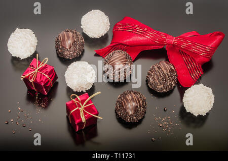 Variation of chocolate truffles and coconut balls with red tied ribbon. Two small brightly Christmas square boxes. Christmas decorations on black back Stock Photo