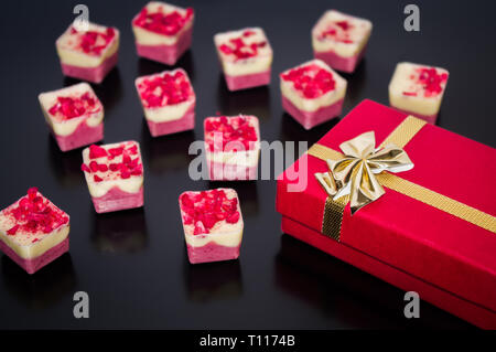 Milk and white belgian chocolates with red gift box with gold ribbon tied into bow. Stock Photo