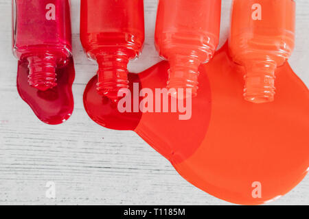 nail polish bottles in different shades of red to orange and purple spilling color on wooden surface, concept of cosmetics industry and manicure Stock Photo