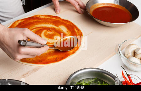 Preparing pizza. Chef spreading tomato sauce in pizzeria Stock Photo