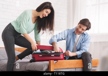 Couple trying to close full suitcase in bedroom