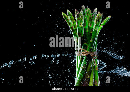 Asparagus in splashes on black background. Close-up. A series of fruits and vegetables in motion. Stock Photo