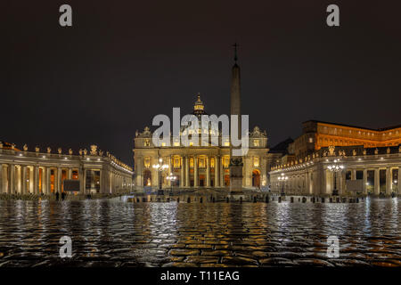 St Peter's Basilica from heart of Vatican. Wet pavement reflects lights of church and Bernini columnade Stock Photo