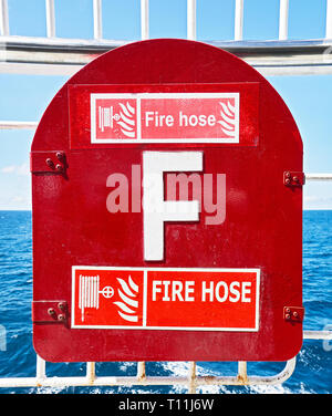 Close-up of a closed red colored repainted fire hose cabinet box attached to the railing, and ocean as background, seen on a ship in the Philippines Stock Photo