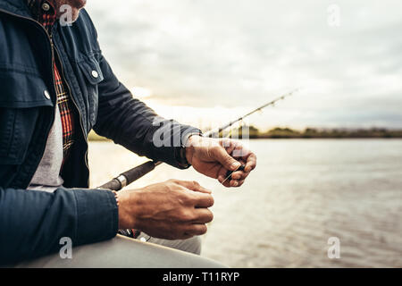 Cropped shot of a person preparing his fishing rod for fishing. Man setting a bait to his fishing rod to catch a fish. Stock Photo