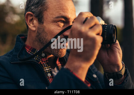 Tourist taking a photo standing outdoors. Close up of a nature lover taking a photo using a camera. Stock Photo