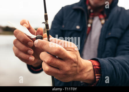 Cropped shot of a man tying a bait to his fishing rod. Close up of hands of a person fixing a bait to a fishing rod to catch fish. Stock Photo