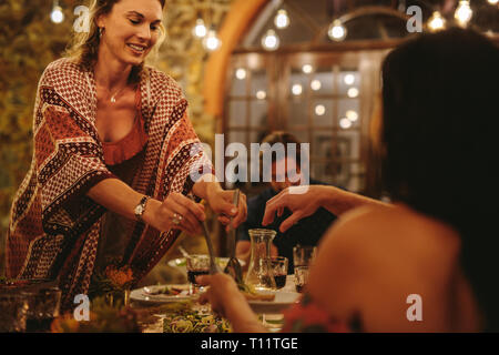 Woman serving food to friends at party. Group of young people having a dinner together outdoors. Stock Photo