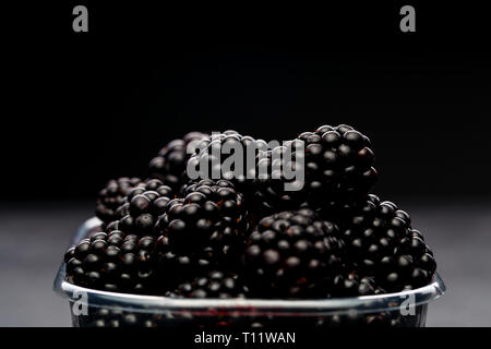 Photo of blackberry in plastic container on empty black background. Stock Photo