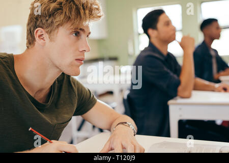 Male student paying attention to the lecture sitting in classroom, with other students in background. Stock Photo