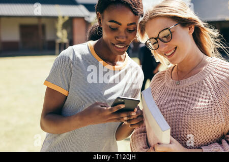 Two young women at college campus looking at mobile phone. High school girls walking in university campus with smart phone.