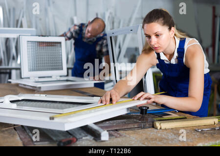 Workwoman is checking dimensions of finished plastic window using measuring tape at factory. Stock Photo