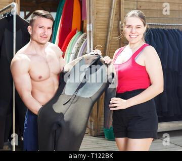 Young sporty couple choosing wetsuit in surf club while planning to surf Stock Photo