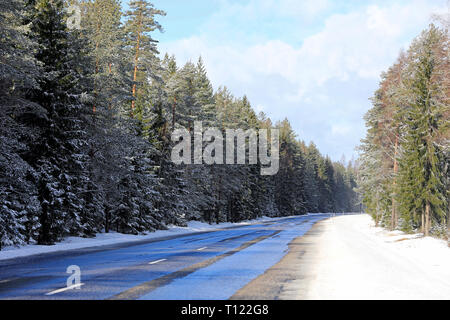 Landscape of a rural highway flanked by forest on a sunny day of winter. Marttila, Finland. Stock Photo