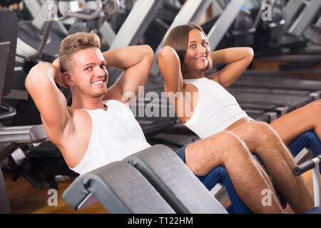 young spanish man and woman making sit ups together using machine in gym Stock Photo