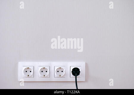 Four power sockets, black lead and plug on the gray wall. Stock Photo