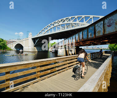 BU Bridge, old railroad and bike path on Charles River. People commuting and rowing, Boston city skyline in background. Massachusetts, USA Stock Photo