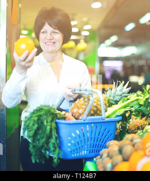 Middle aged woman with basket choosing fruits and vegetables on the market Stock Photo