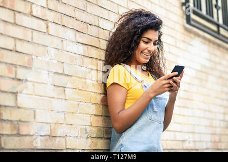 Young North African woman texting with her smart phone outdoors Stock Photo