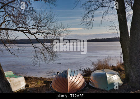 Upturned boats on shores of a frozen Lake Malaren with long distance ice skaters, Sweden, Scandinavia Stock Photo