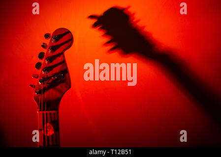 guitar leaning against the wall projects shadow, red colored background Stock Photo