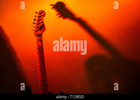 guitar leaning against the wall projects shadow, red colored background Stock Photo