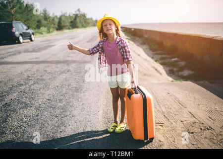 Pretty young hitchhiking little girl along a road. Stock Photo