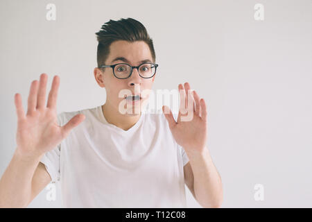 Omg No way Very shocked young man with glasses is looking at the camera. Student nerd is wearing in a white t-shirt, standing isolated on a white back Stock Photo