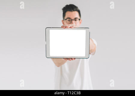 Nerd is wearing glasses holds the white empty screen tablet device.. A man in a white T-shirt is standing on a white background. Stock Photo