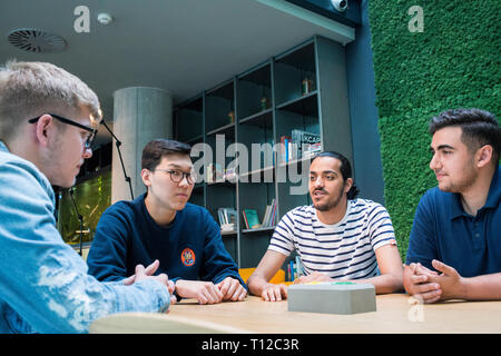 A group of young people sitting around a table chatting with each other. Stock Photo