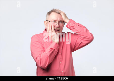 Senior man in red shirt suffering from tooth pain. Stock Photo