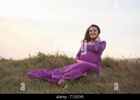 Happy smiling pregnant woman sit on grass Stock Photo