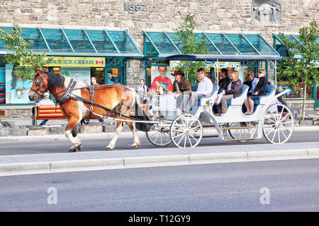 BANFF, CANADA - JULY 3, 2011: Tourists on a horse drawn carriage ride through Banff Avenue in the Canadian Rockies of Alberta. The townsite is a major Stock Photo